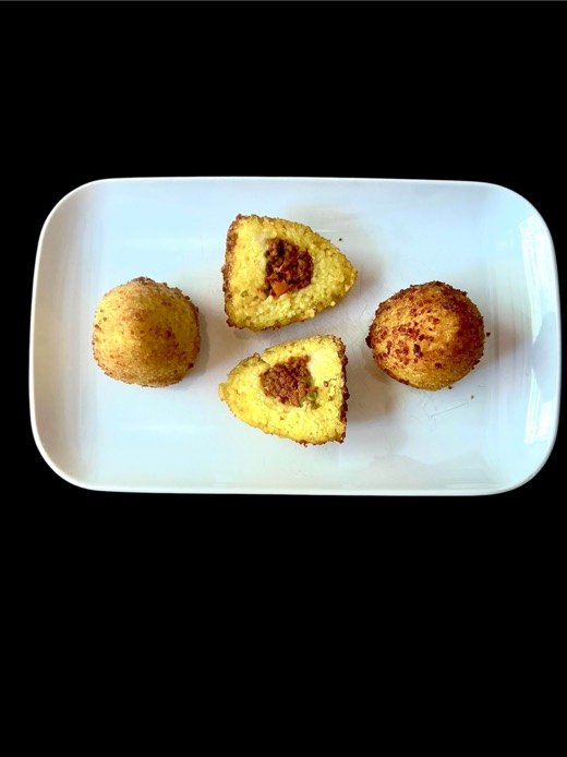 Vier Arancine auf einem weissen Teller, eine davon aufgeschnitten mit Ragù-Füllung.